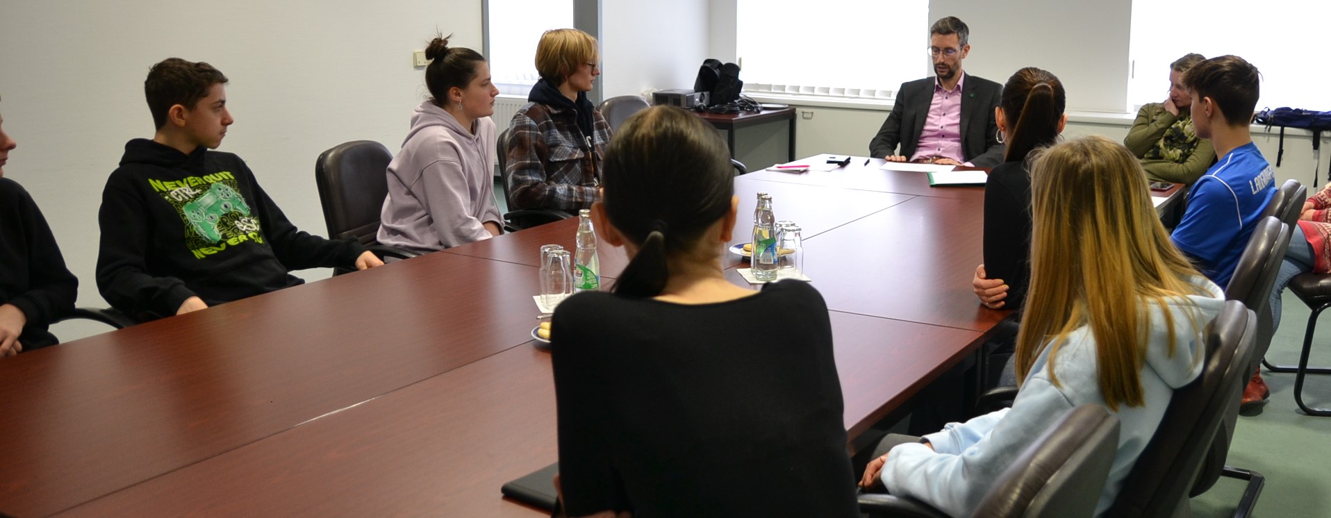 KI generiert: Eine Gruppe von Menschen sitzt um einen Konferenztisch in einem Büro. Sie beteiligen sich an einer Besprechung oder Diskussion.