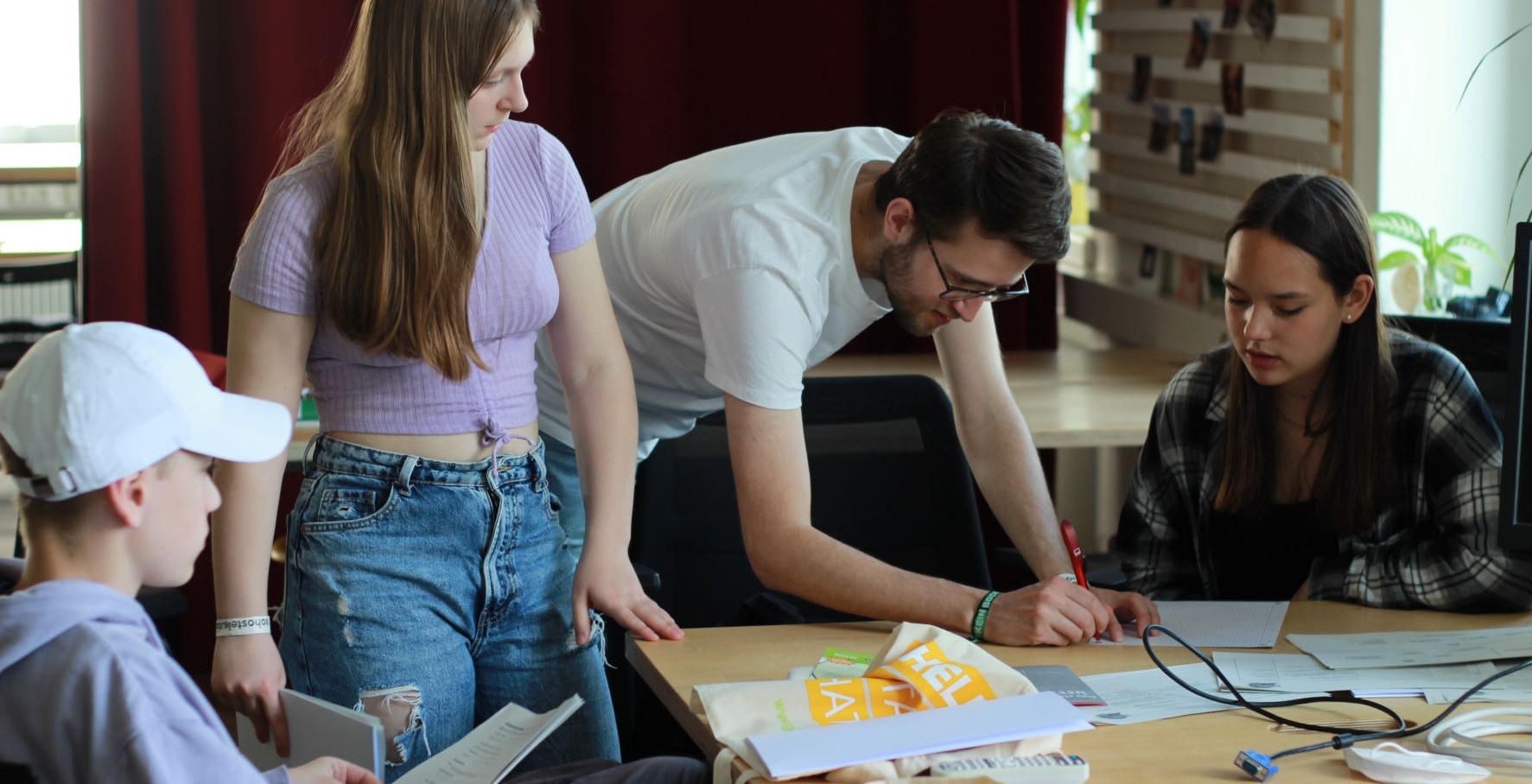 KI generiert: Das Bild zeigt vier junge Menschen, die gemeinsam an einem Tisch arbeiten, wobei eine Person etwas aufschreibt und die anderen zuschauen oder diskutieren. Der Fokus liegt auf der Zusammenarbeit und dem Austausch von Ideen in einer informellen Umgebung.