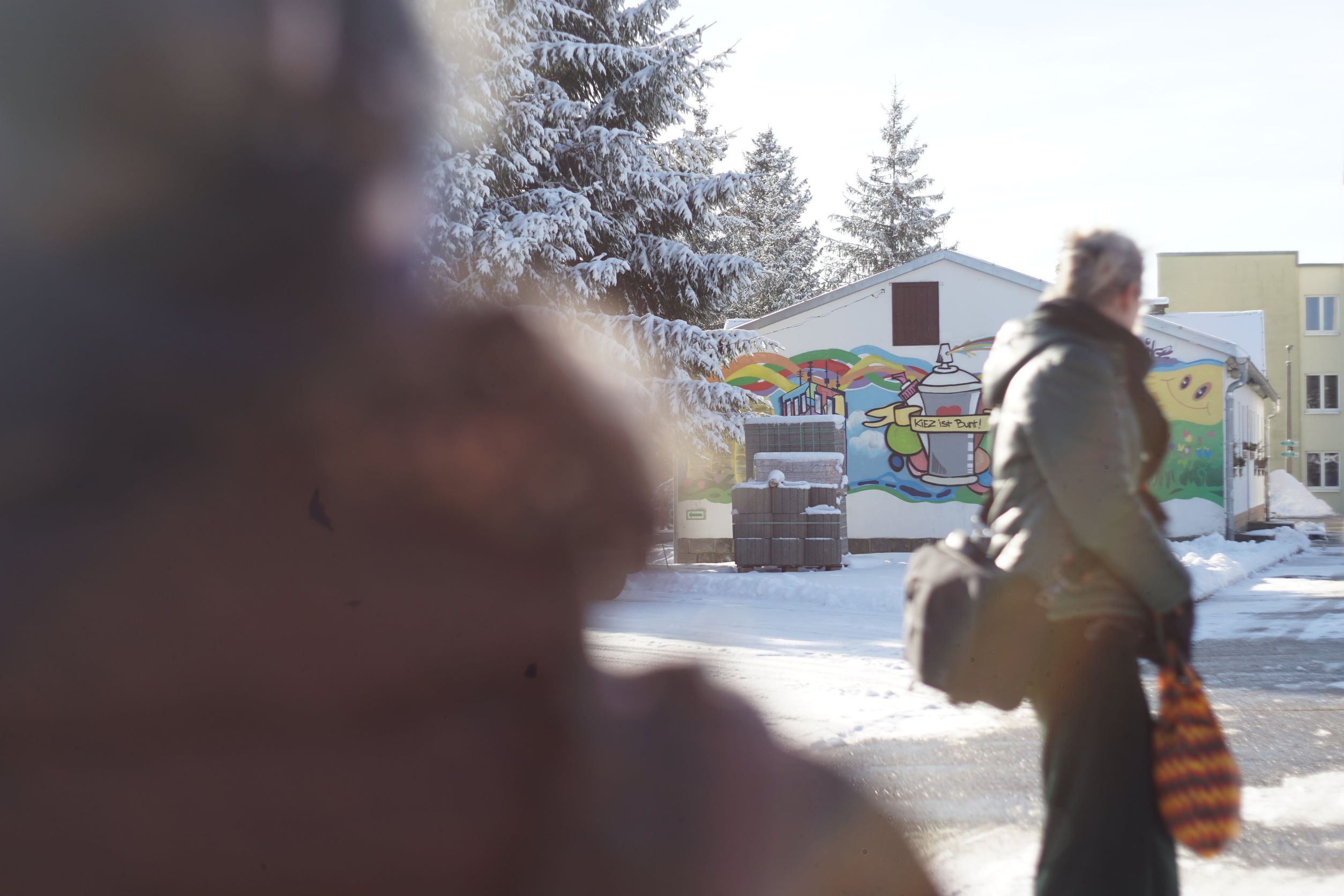KI generiert: Im Bild sieht man eine winterliche Straße mit einem Gebäude im Hintergrund, das mit buntem Graffiti verziert ist, darunter eine Spraydose und die Worte "keep your talent". Vordergrund und ein Teil des Bildes sind unscharf, während eine Person zu sehen ist, die an der Szenerie vorbeigeht.