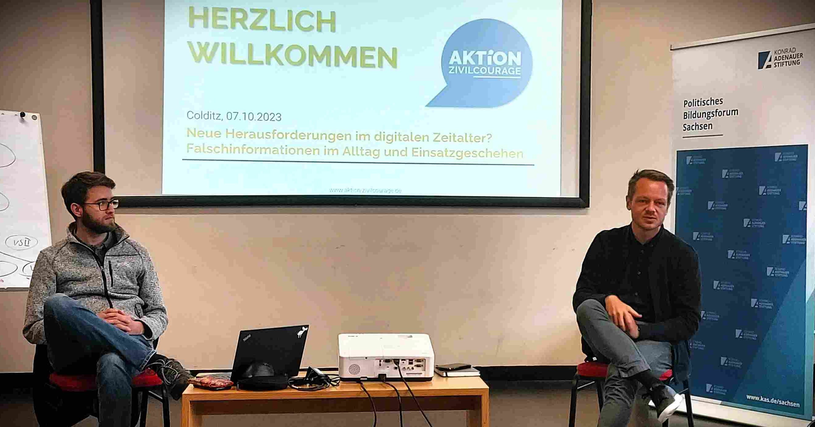 KI generiert: Das Bild zeigt zwei Personen, die an einer Präsentation über Herausforderungen und Falschinformationen im digitalen Zeitalter teilnehmen. Der Hintergrund zeigt eine Leinwand mit dem Titel der Veranstaltung und das Logo der Aktion Zivilcourage.