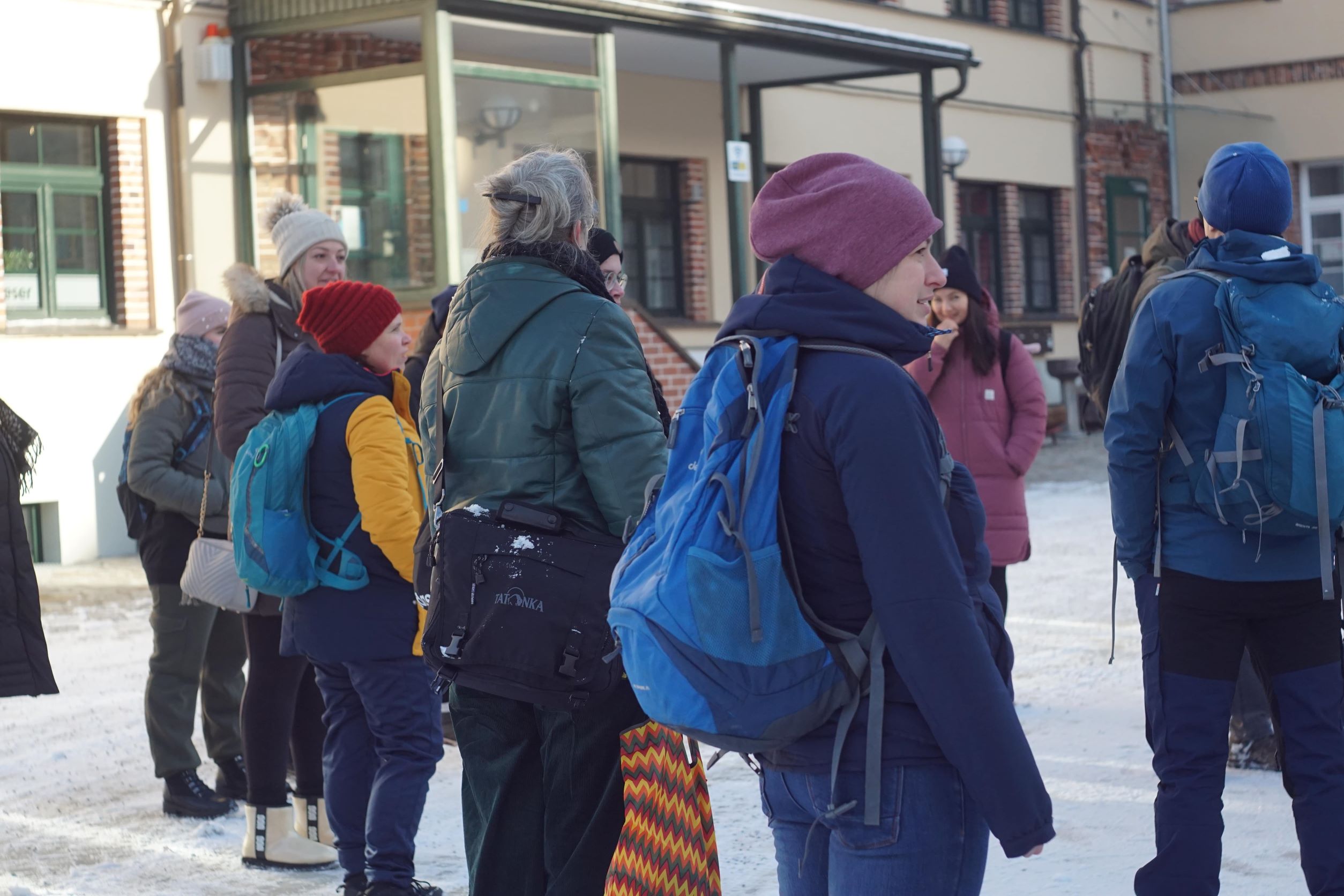 KI generiert: Eine Gruppe von Menschen steht im Freien bei winterlichen Bedingungen, viele tragen warme Kleidung und Rucksäcke. Sie scheinen in ein Gespräch oder eine Aktivität vertieft zu sein.