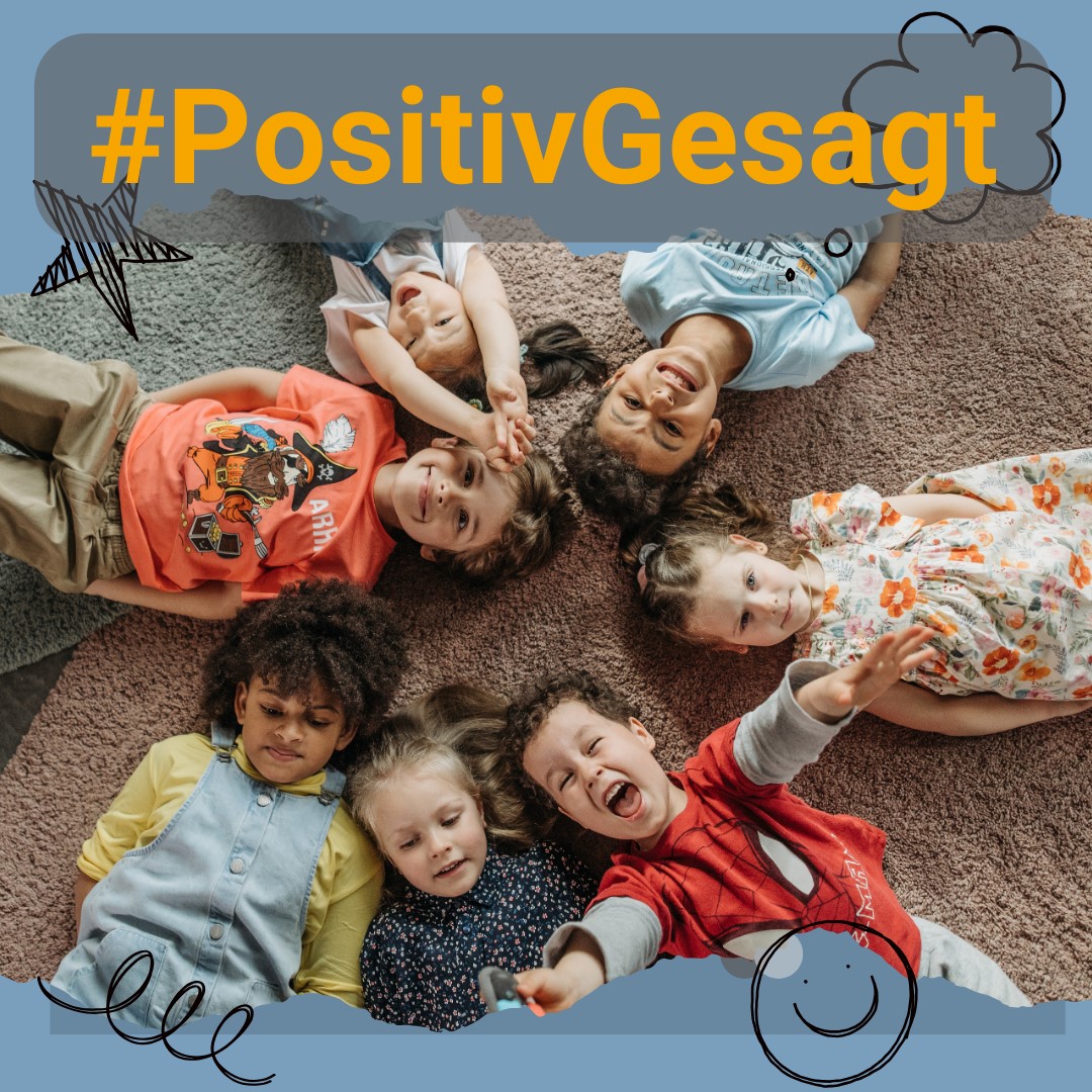 KI generiert: Das Bild zeigt mehrere fröhliche Kinder, die in einem Kreis auf dem Boden liegen und in die Kamera lächeln. Der Hashtag "#PositivGesagt" steht prominent darüber.
