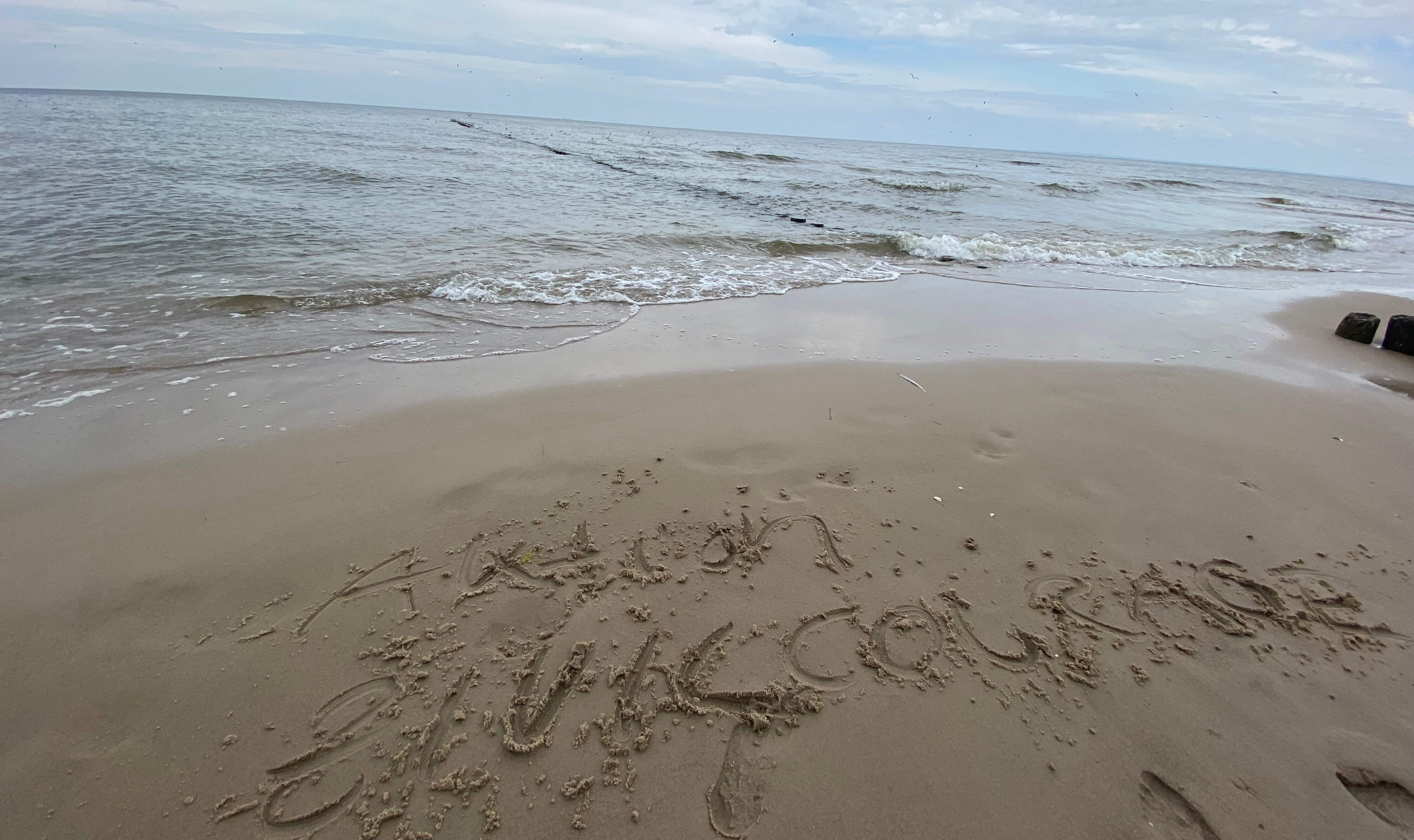 KI generiert: Auf dem Bild sieht man einen Strand mit Wellen, die sanft an das Ufer schlagen. Im Sand ist eine Nachricht geschrieben.